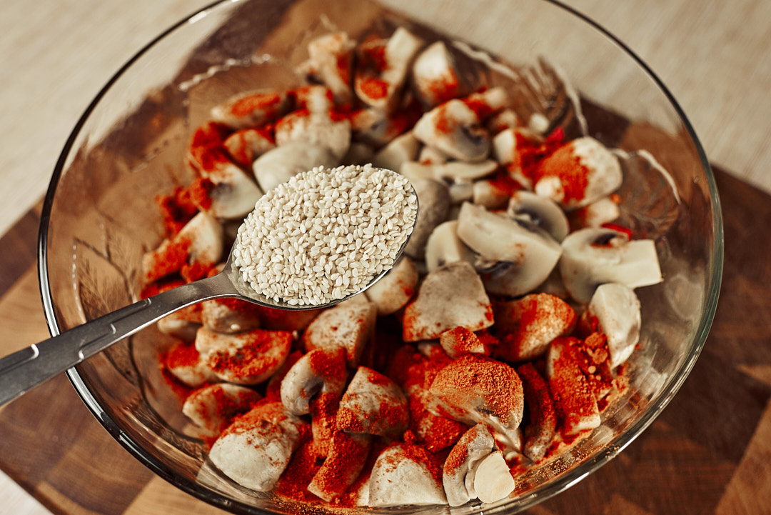 Sprinkling sesame seeds over mushrooms with paprika