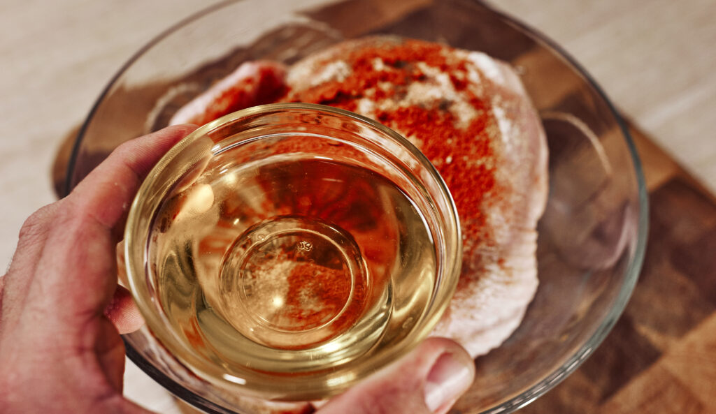 pouring oil over seasoned chicken