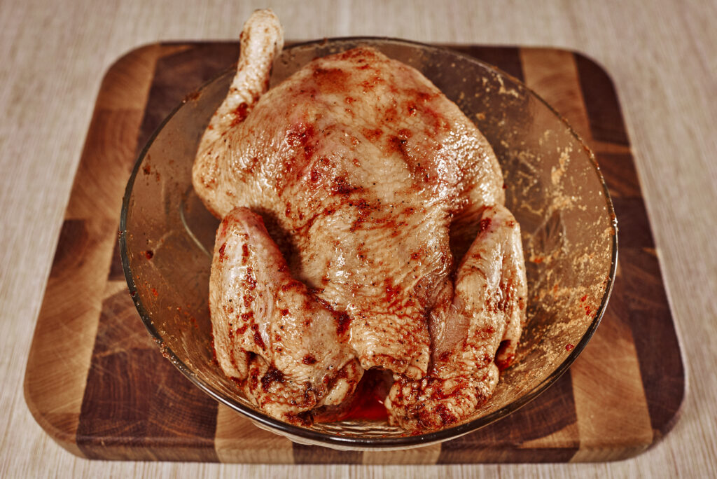 whole chicken coated with garlic, salt, paprika, and black pepper ready for oven baking