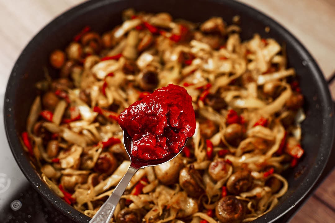 Stirring in tomato paste with cabbage and mushrooms