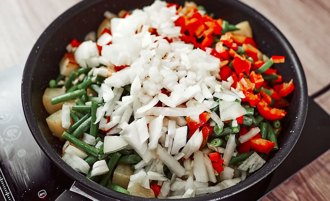 Cooking green beans and potatoes with bell pepper and garlic in a skillet