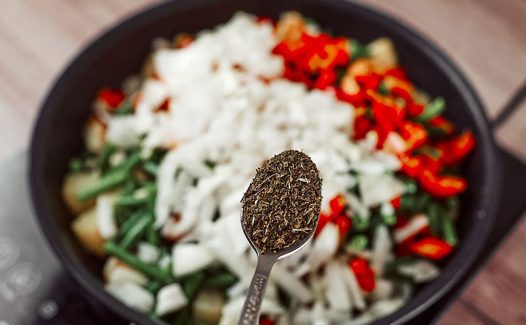 Seasoning vegan green beans and potatoes stew with black pepper and herbs