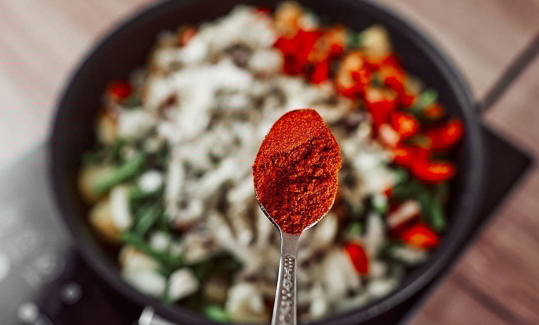 Sprinkling salt, black pepper, thyme, and paprika over green beans and potatoes while cooking