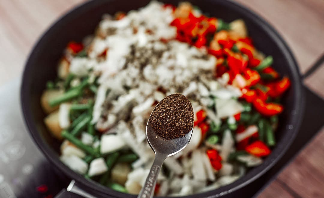 Seasoning vegan green beans and potatoes stew with black pepper and herbs