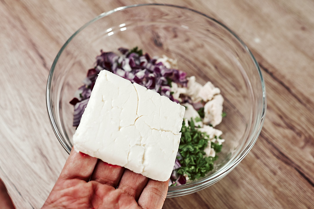 Crumbling feta cheese into keto chicken salad