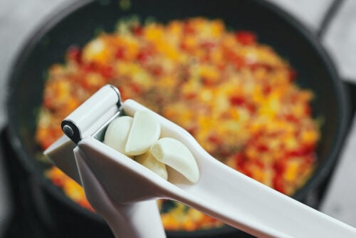 Adding minced garlic and dried herbs to sautéed vegetables in a skillet