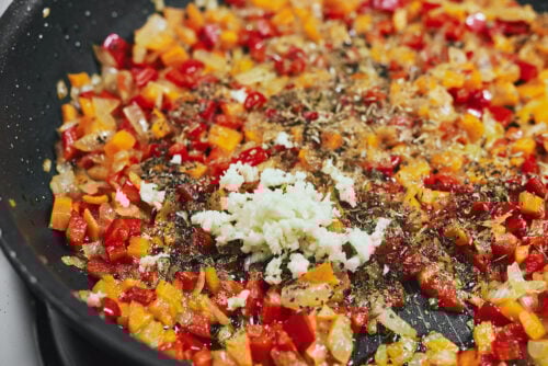 Garlic, oregano, and basil sizzling with vegetables in the skillet
