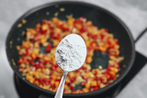 Sprinkling flour over sautéed vegetables to thicken the sauce