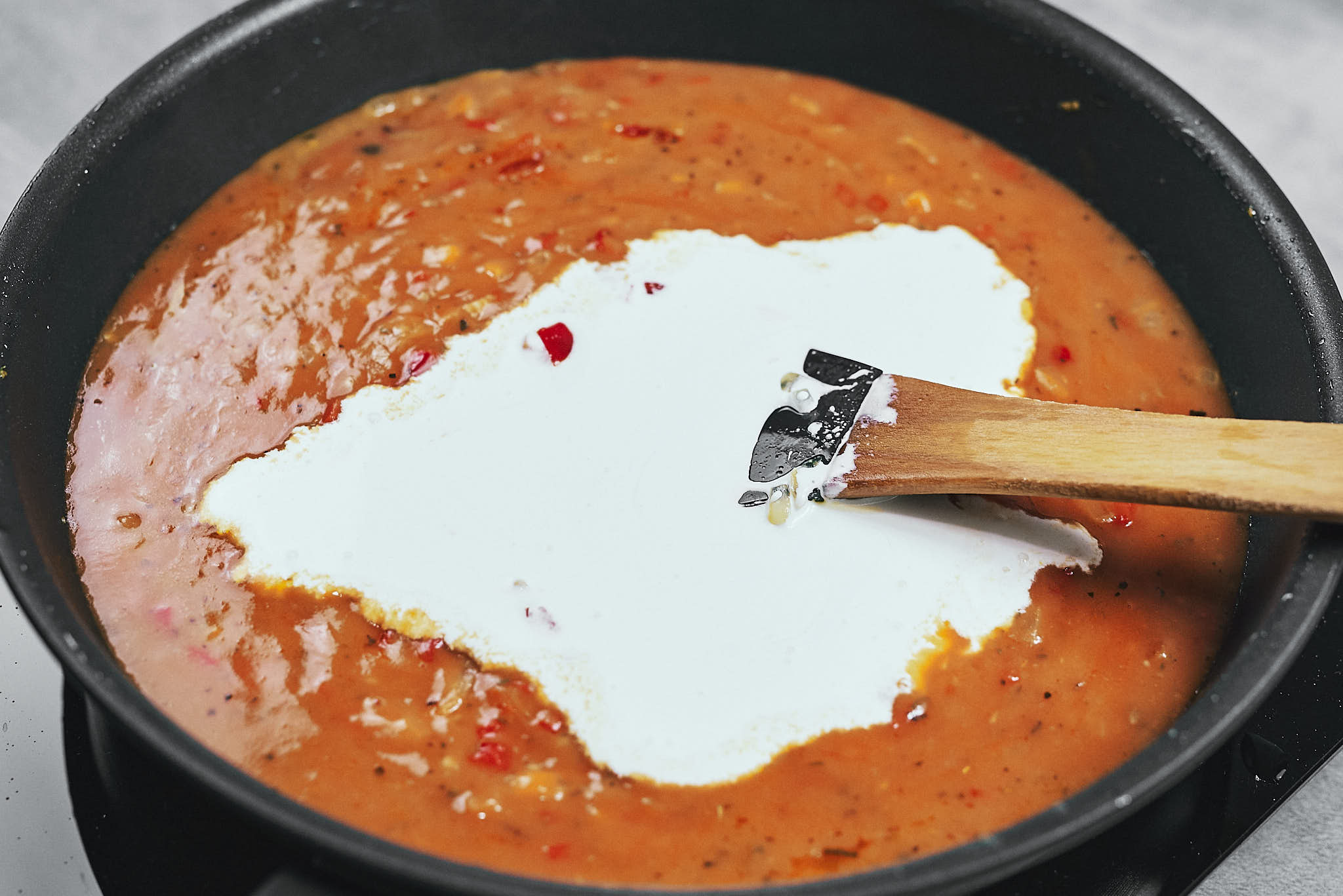 Pouring heavy cream into the tomato base to make the sauce creamy