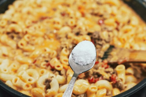 Adding salt to the creamy meat sauce in the skillet