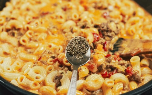 Adding black pepper to the creamy pasta meat sauce in the skillet