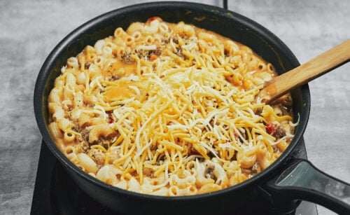 Adding shredded cheese to the creamy pasta in the skillet