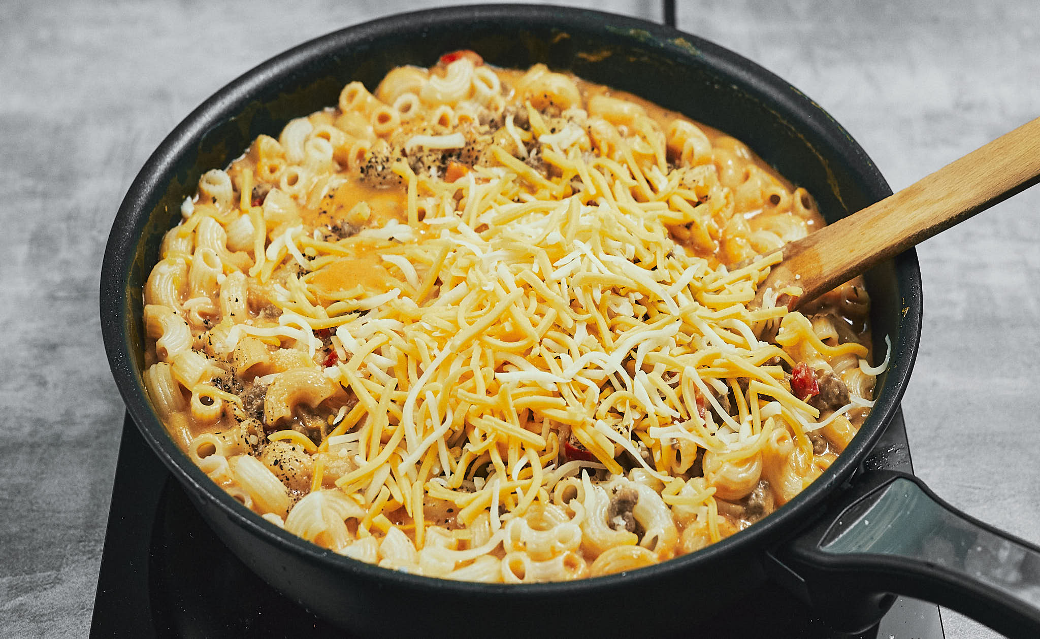 Adding shredded cheese to the creamy pasta in the skillet
