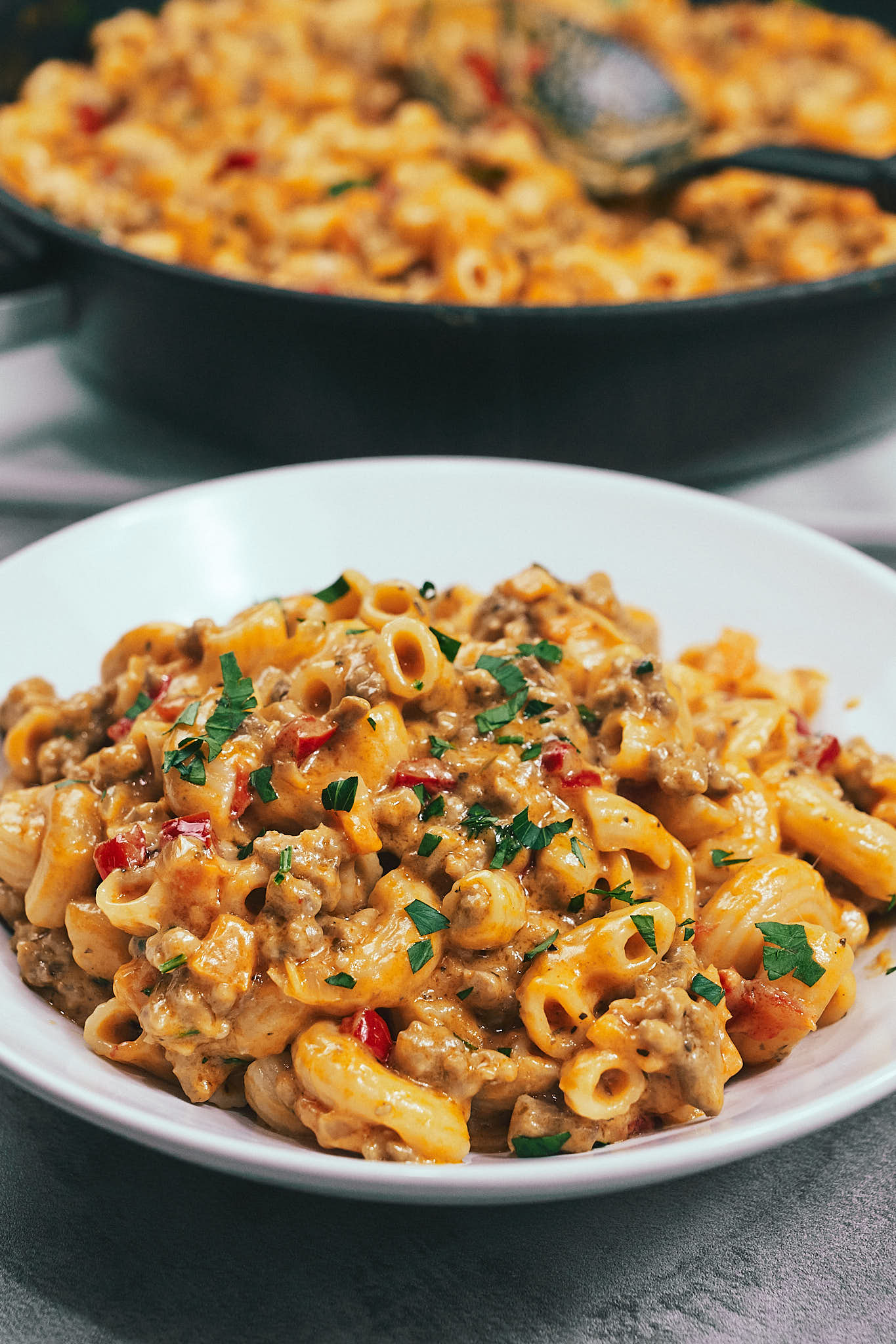 Creamy cheesy tomato pasta served in a skillet with ground meat and vegetables