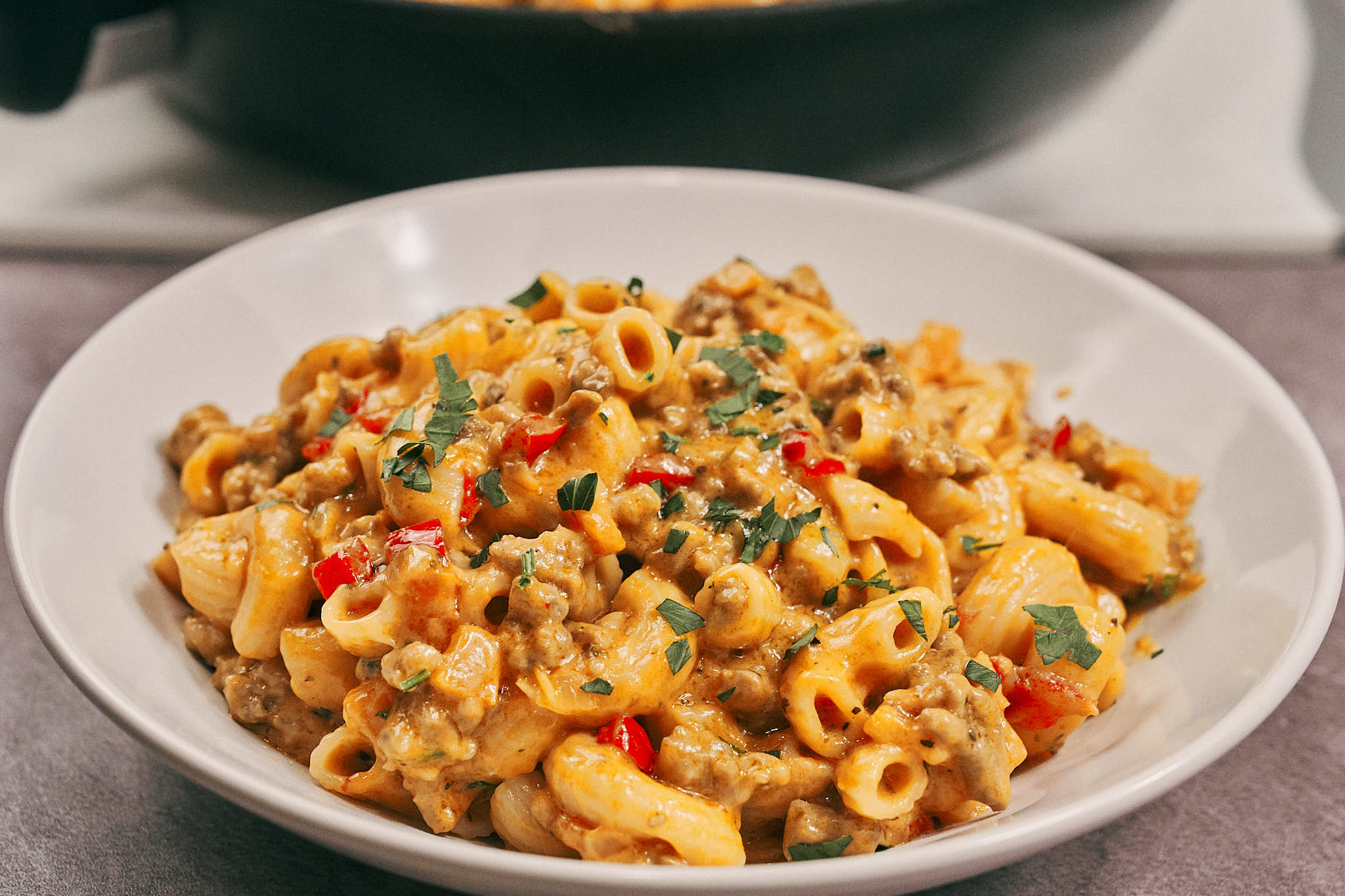 Creamy cheesy tomato pasta with ground meat and bell peppers served in a white bowl