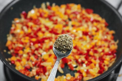Adding oregano to sautéed vegetables in a skillet