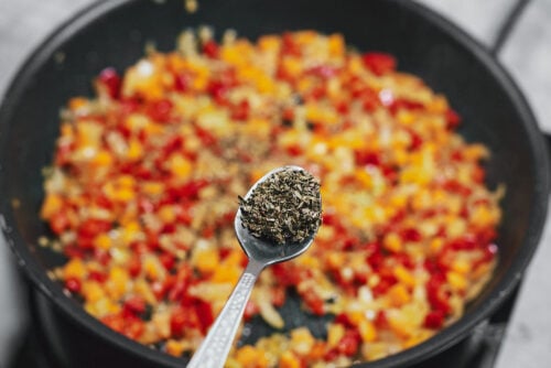 Adding basil to sautéed vegetables in a skillet