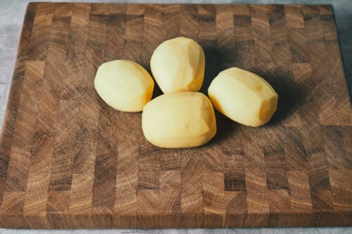 Peeled potatoes on a cutting board ready for cooking