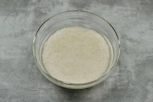 Rice soaking in hot water and uncooked rice measured for the cabbage rolls filling preparation.