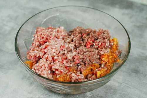 Ground beef and pork added to sautéed vegetables in a mixing bowl.