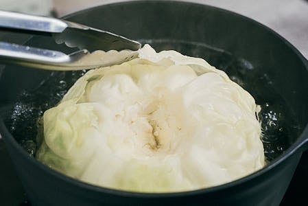 Whole cabbage boiling in a pot to soften the leaves for cabbage rolls.