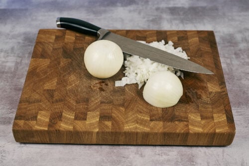 Chopped onions on a cutting board with a knife.