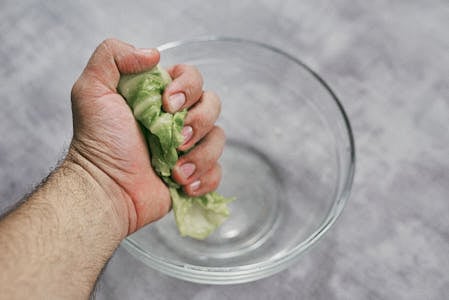 Hand squeezing boiled cabbage leaf to remove excess water.