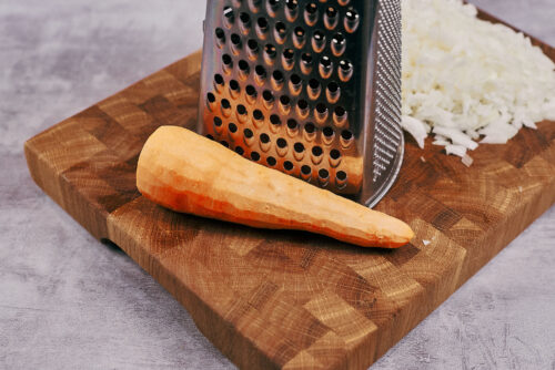 Carrot and onions being grated on a box grater