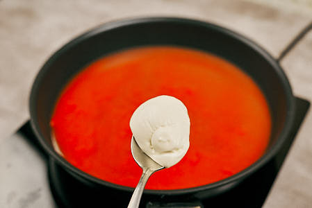 Sour cream being added to tomato sauce in a saucepan.