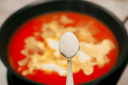 Sugar being added to the tomato and sour cream sauce.