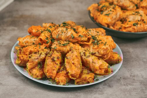 Easy stuffed cabbage rolls with rice, beef, and pork served on a plate with tomato sauce and fresh herbs.