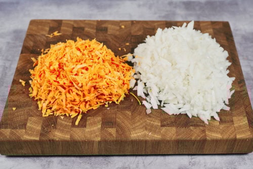 Grated carrot and finely chopped onion on a wooden board.