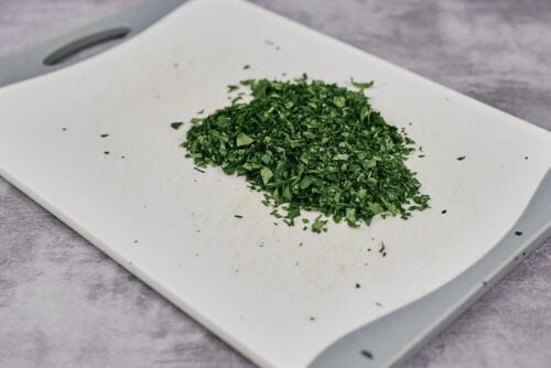 Finely chopped fresh parsley on a white cutting board.