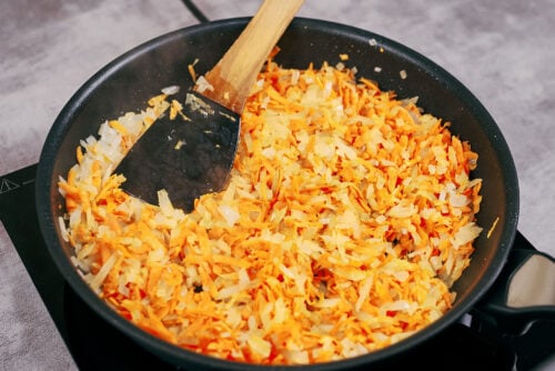 Onions and carrots sautéing in a pan with oil