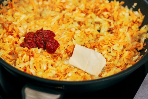 Tomato paste and butter added to sautéed onions and carrots in a pan.