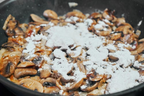 Stirring flour into mushrooms to thicken beef stroganoff