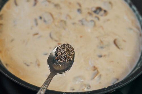 Adding black pepper to creamy beef stroganoff sauce