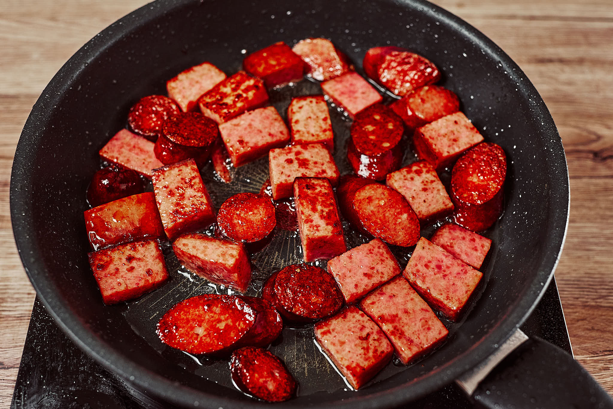 Smoked sausage pieces browning in a hot skillet until golden and crispy.