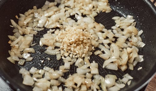 Minced garlic added to sautéed onions in a skillet, cooking briefly.