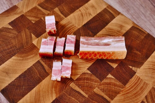 Sliced bacon pieces on a wooden cutting board, ready for cooking.