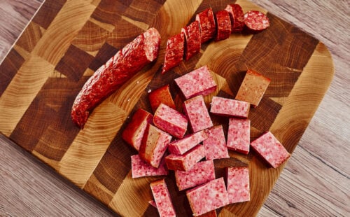 Smoked sausages sliced into cubes and rounds on a wooden cutting board, ready for cooking.