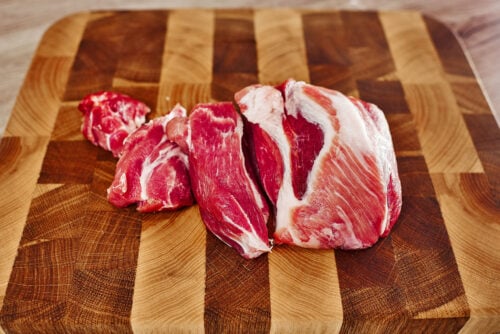 Raw pork pieces on a wooden cutting board, prepared for the bean stew.