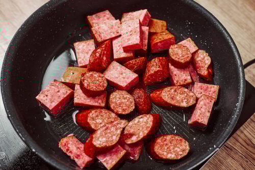 Pieces of smoked sausage placed in a skillet before browning.