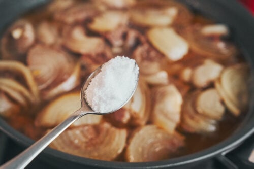 Salt being added to simmering beef and onions