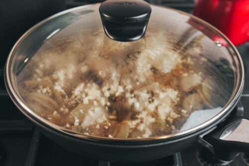 Covered skillet with garlic butter beef simmering on low heat
