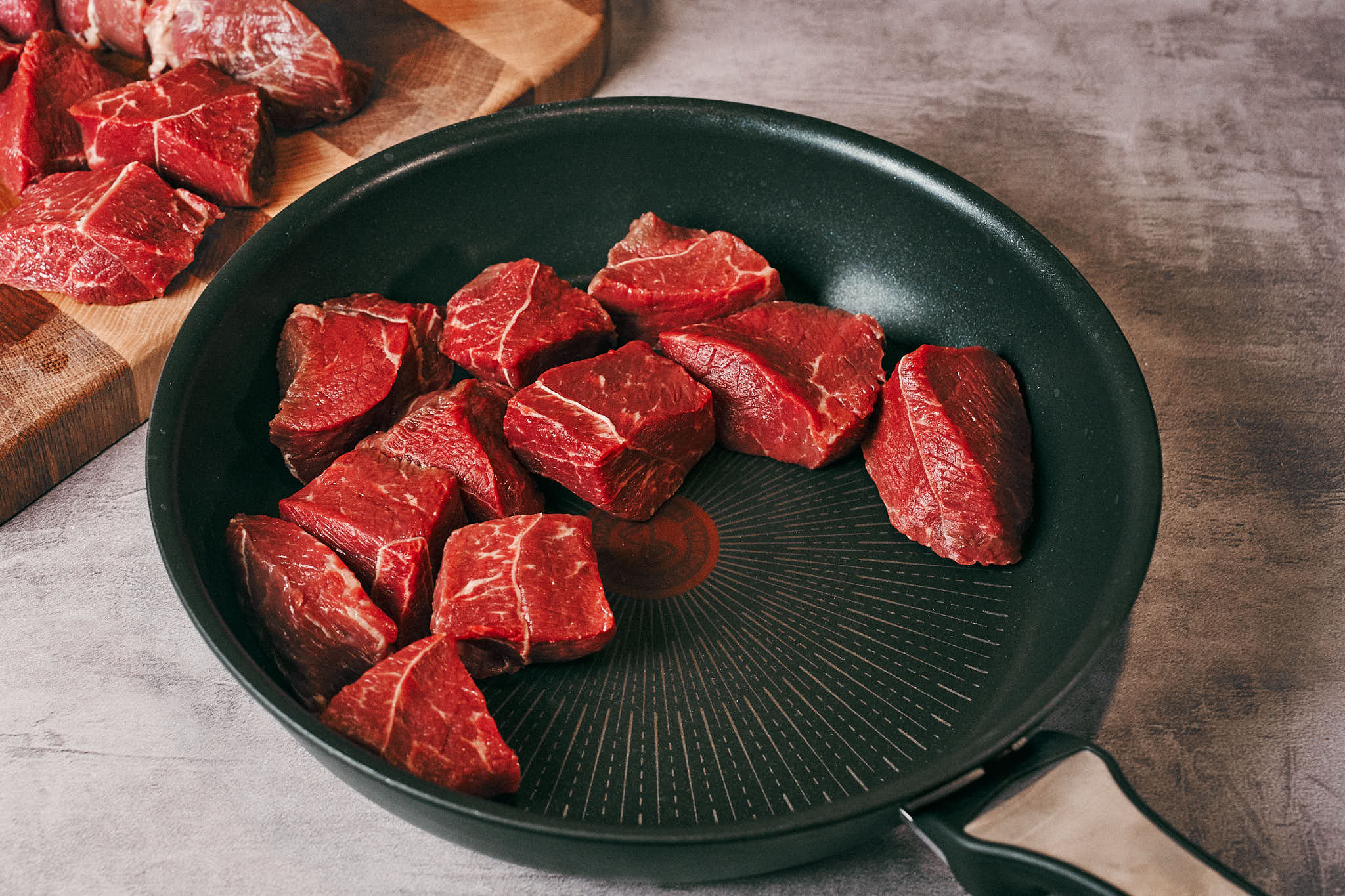 Cubed beef chuck arranged in a skillet for slow simmering