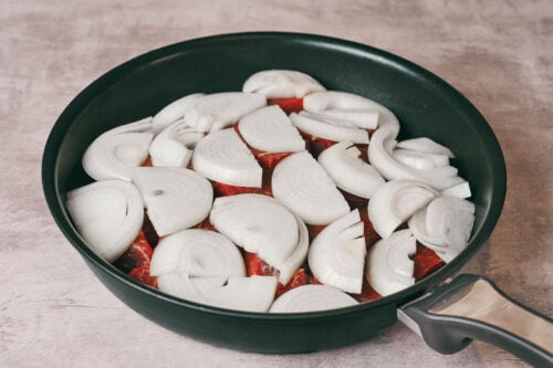 Sliced onions layered over beef in a skillet