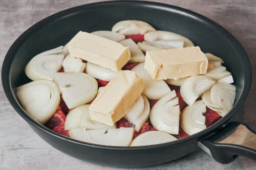 Butter placed over onions and beef in a skillet