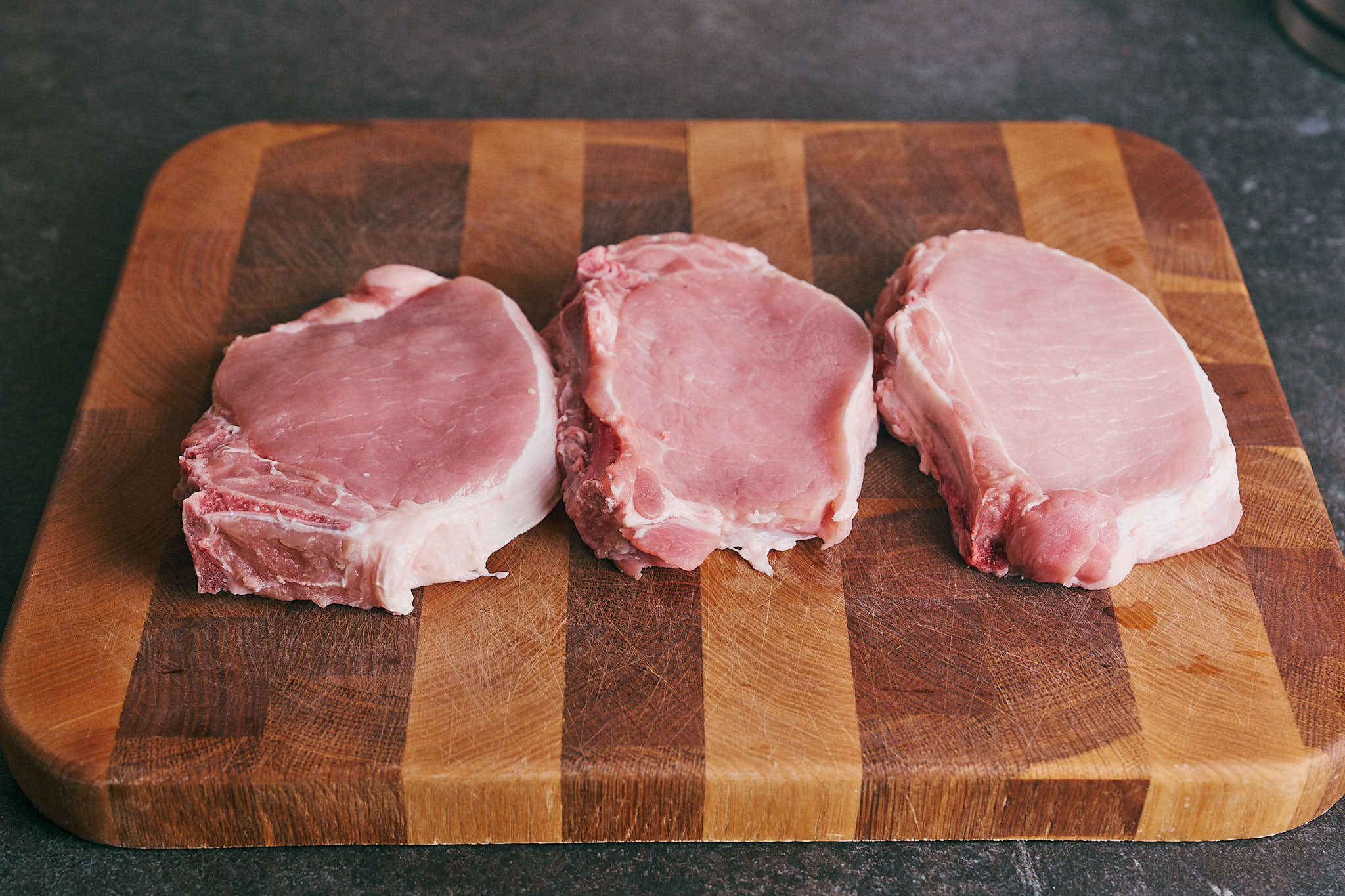 Raw bone-in pork chops on a wooden cutting board