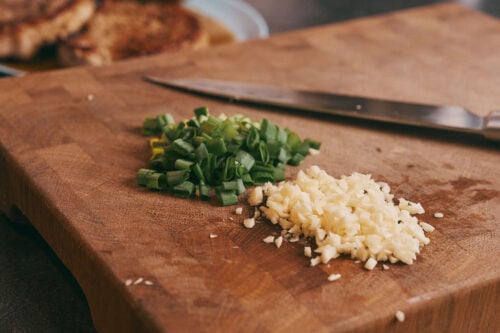 Chopped green onion and minced garlic on a cutting board